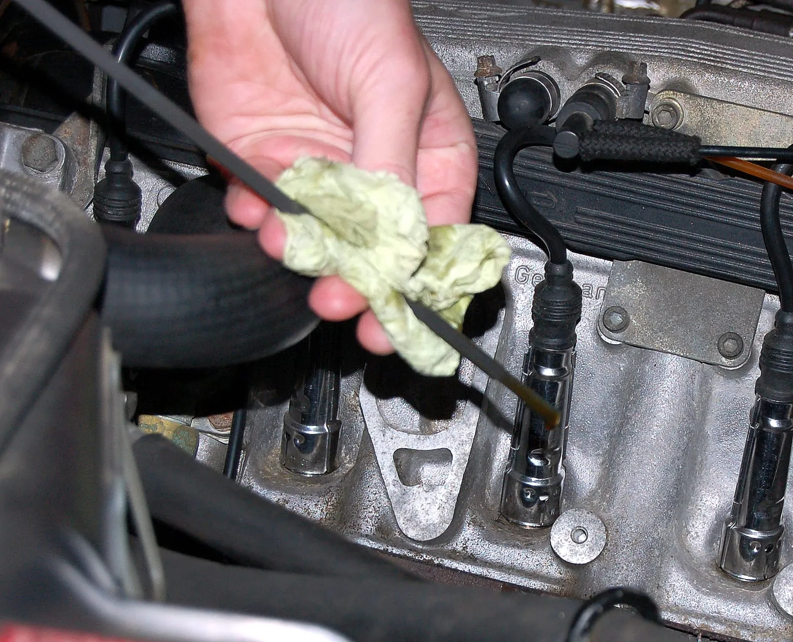 Mano que limpia con un trapo la varilla medidora de aceite, junto al motor de un auto.